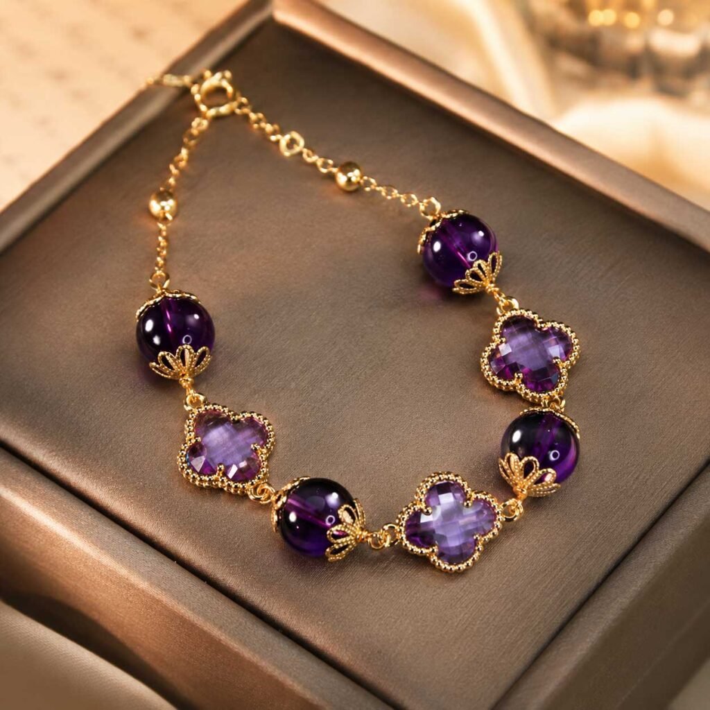 Close-up of a premium handcrafted lucky charm bracelet featuring deep translucent purple amethyst beads and a polished four-leaf clover charm, 24h sound-bath calibrated at 528Hz, showcased inside the signature white Luxe Abundance Box.